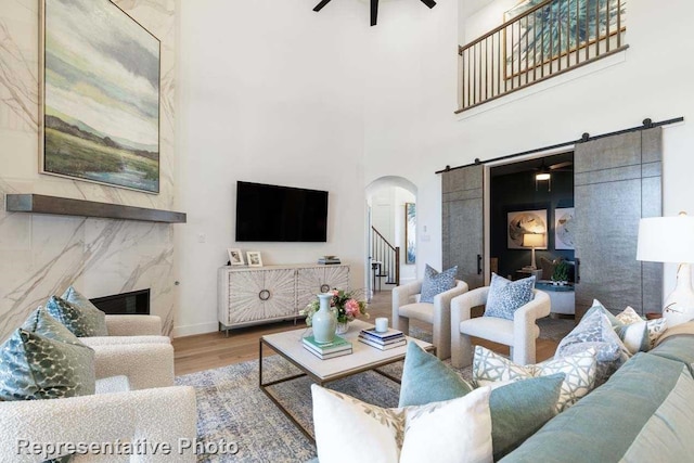 living room featuring ceiling fan, a barn door, a towering ceiling, a fireplace, and wood-type flooring