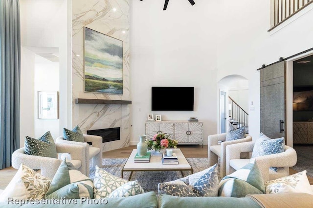 living room featuring hardwood / wood-style floors, ceiling fan, a barn door, a towering ceiling, and a fireplace