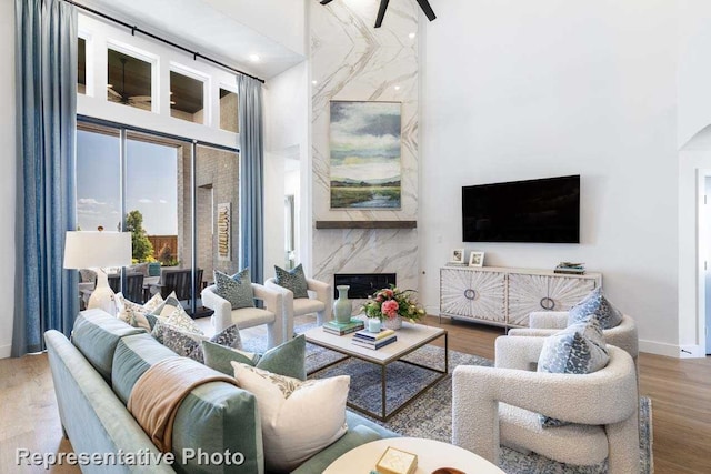 living room with a high end fireplace, wood-type flooring, and a high ceiling