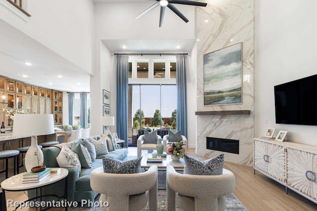 living room with ceiling fan, light hardwood / wood-style floors, a fireplace, and a high ceiling