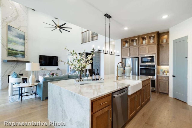 kitchen featuring appliances with stainless steel finishes, a kitchen island with sink, sink, decorative light fixtures, and light hardwood / wood-style floors