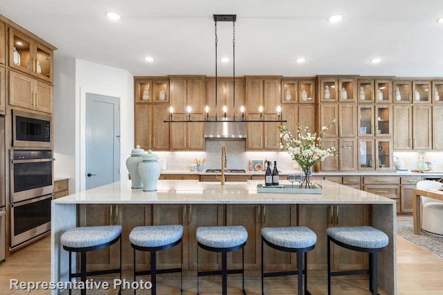 kitchen with a large island with sink, pendant lighting, light hardwood / wood-style floors, and range hood