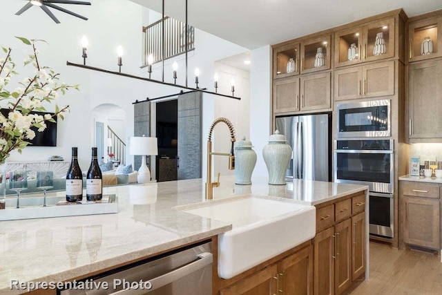 kitchen with sink, light stone counters, light hardwood / wood-style flooring, pendant lighting, and appliances with stainless steel finishes