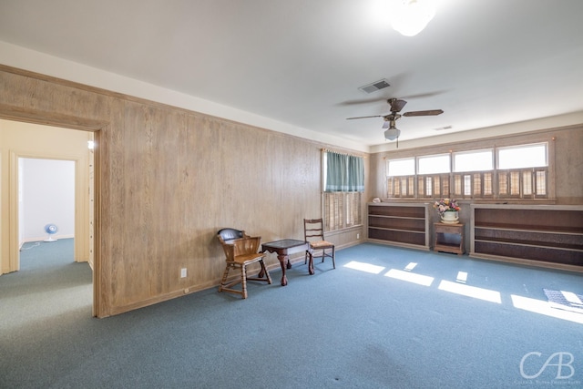 sitting room featuring carpet flooring, ceiling fan, and wooden walls