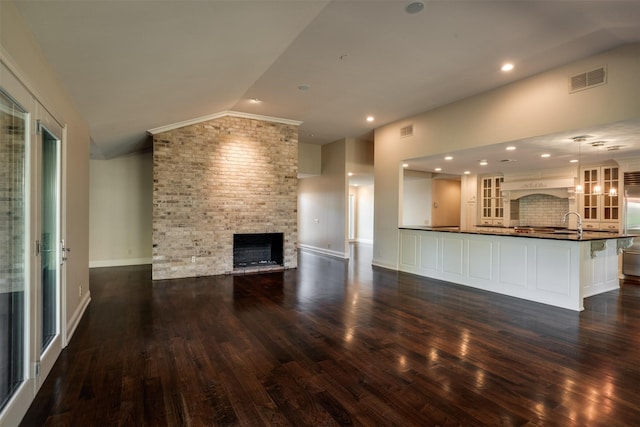 2516 Beefeater Dr, Wichita Falls, TX 76308 - unfurnished living room with vaulted ceiling, a brick fireplace, dark wood-style floors, and recessed lighting