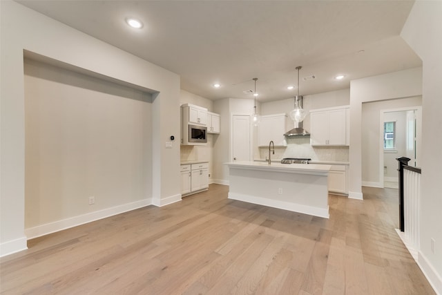 kitchen featuring pendant lighting, a center island with sink, sink, light hardwood / wood-style flooring, and white cabinetry