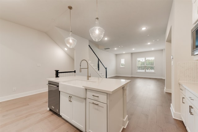 kitchen with white cabinets, sink, an island with sink, decorative light fixtures, and light hardwood / wood-style floors