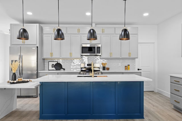 kitchen with hanging light fixtures, appliances with stainless steel finishes, light stone countertops, and a kitchen island with sink