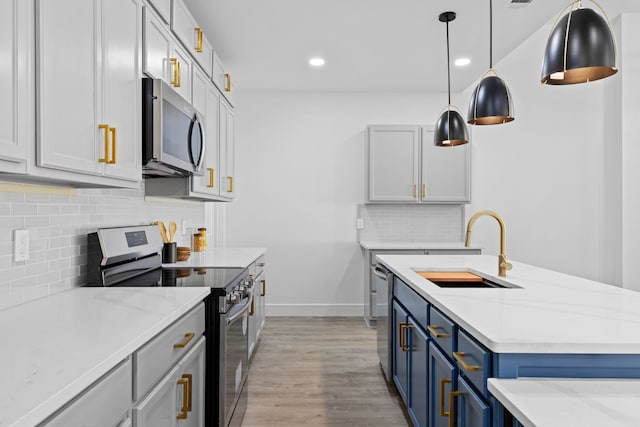 kitchen with pendant lighting, sink, light hardwood / wood-style flooring, blue cabinetry, and appliances with stainless steel finishes