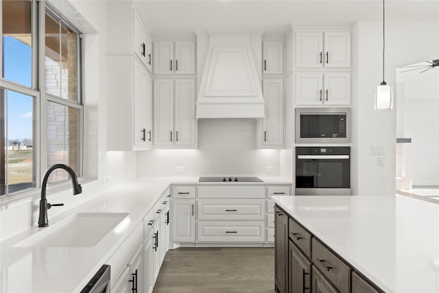 kitchen with custom range hood, sink, black appliances, white cabinetry, and hanging light fixtures