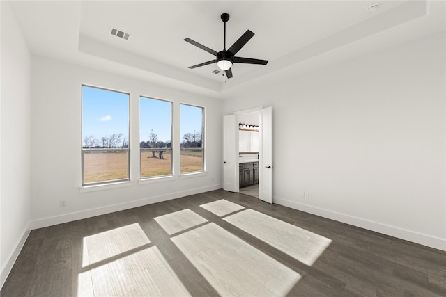 unfurnished bedroom featuring a tray ceiling, ceiling fan, dark hardwood / wood-style flooring, and ensuite bathroom