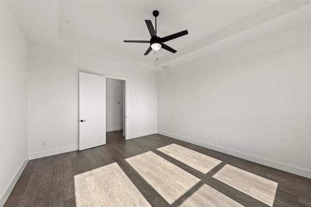 unfurnished bedroom with a tray ceiling, ceiling fan, and dark hardwood / wood-style floors