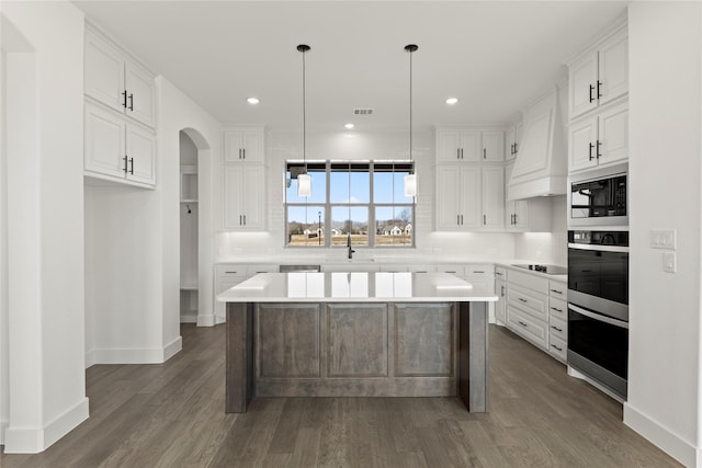 kitchen featuring custom exhaust hood, dark wood-type flooring, pendant lighting, a center island, and white cabinetry