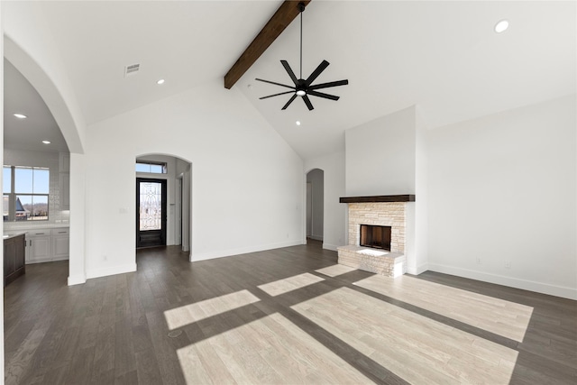 unfurnished living room featuring a stone fireplace, a wealth of natural light, beamed ceiling, and high vaulted ceiling