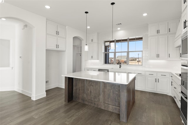 kitchen with backsplash, white cabinets, decorative light fixtures, a kitchen island, and dark hardwood / wood-style flooring