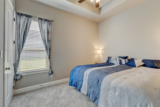 carpeted bedroom with a raised ceiling and ceiling fan