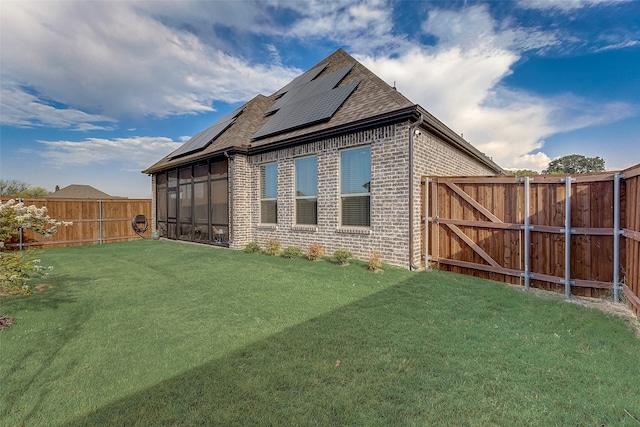 rear view of house with solar panels, a sunroom, and a lawn