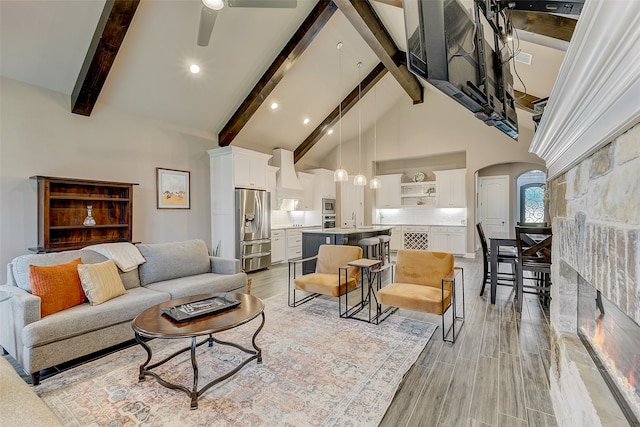 living room with high vaulted ceiling, sink, ceiling fan, beam ceiling, and light hardwood / wood-style floors