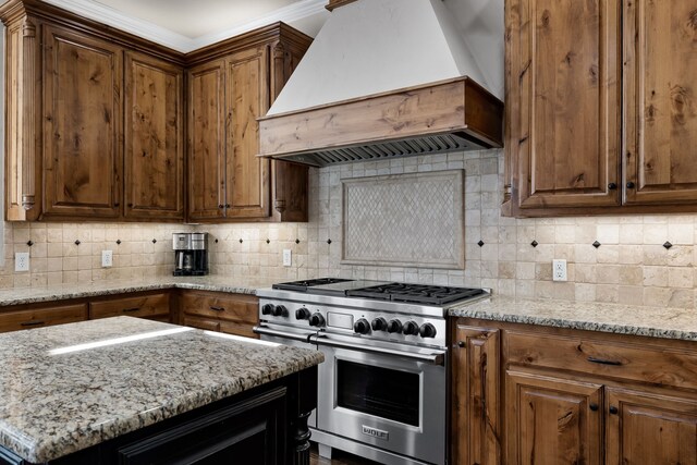 kitchen with stainless steel range, decorative backsplash, premium range hood, and light stone countertops