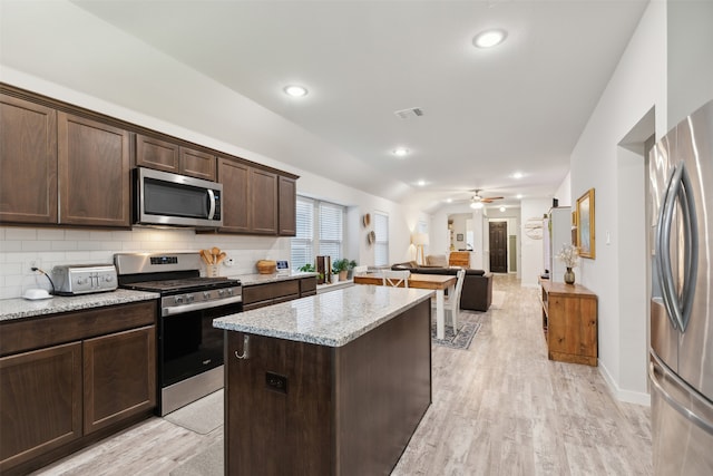 kitchen with appliances with stainless steel finishes, light hardwood / wood-style flooring, light stone counters, and dark brown cabinets