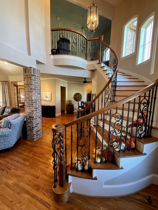 stairs featuring a high ceiling, decorative columns, an inviting chandelier, and hardwood / wood-style flooring