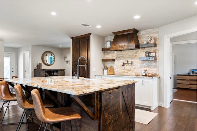 kitchen featuring a kitchen breakfast bar, dark hardwood / wood-style flooring, light stone counters, white cabinetry, and a large island