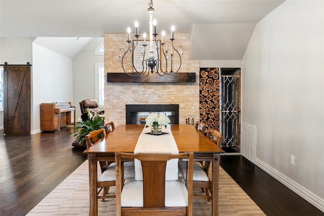 dining space with lofted ceiling, a stone fireplace, a barn door, a notable chandelier, and dark hardwood / wood-style flooring