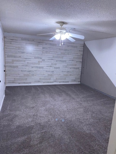 bonus room with ceiling fan, wood walls, a textured ceiling, and dark carpet