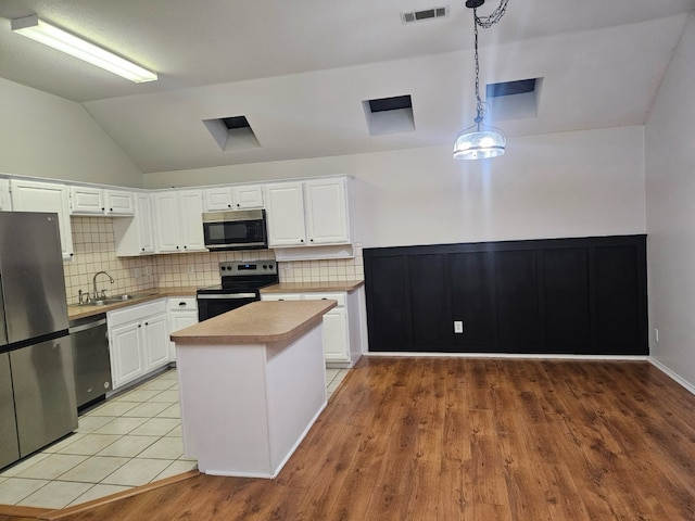 kitchen featuring stainless steel appliances, vaulted ceiling, decorative light fixtures, decorative backsplash, and white cabinets