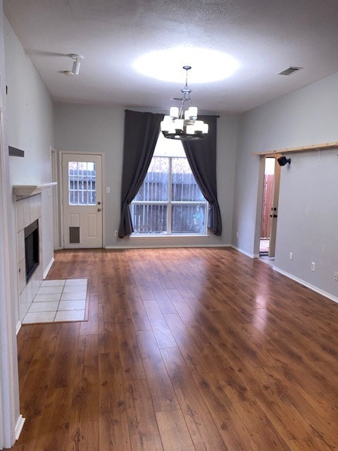 unfurnished living room featuring a notable chandelier, dark hardwood / wood-style flooring, and a tile fireplace