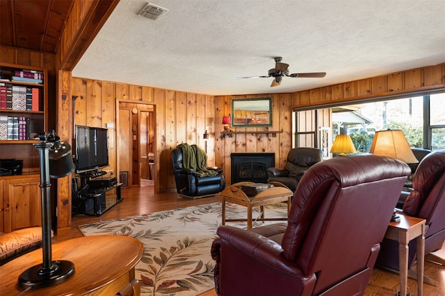 living room with wooden walls, light hardwood / wood-style flooring, ceiling fan, and a textured ceiling