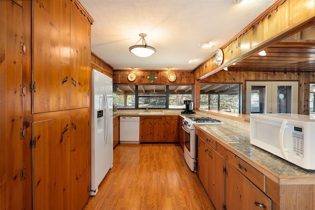 kitchen with french doors, sink, light hardwood / wood-style floors, white appliances, and wooden walls