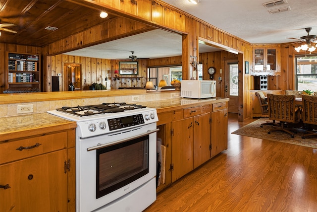 kitchen with a textured ceiling, white appliances, light hardwood / wood-style flooring, and wooden walls