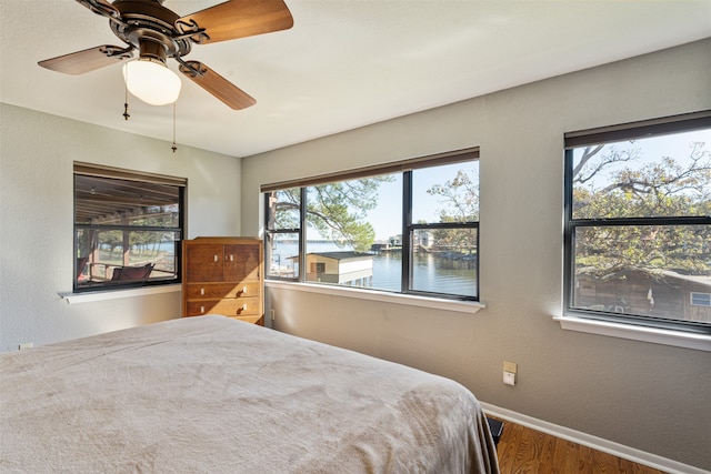 bedroom featuring ceiling fan, a water view, wood-type flooring, and multiple windows