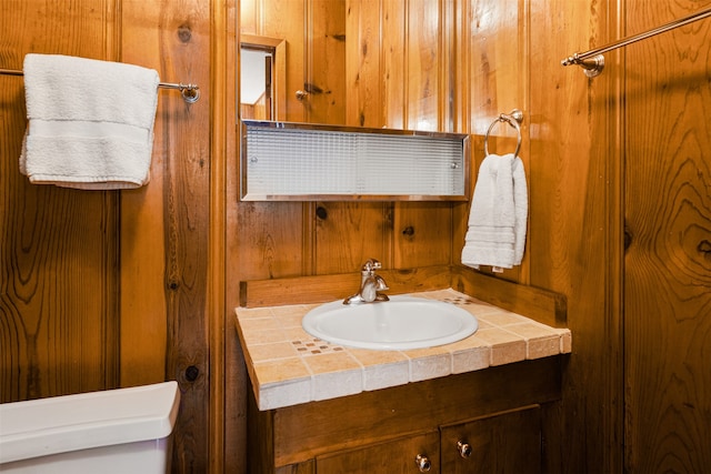 bathroom featuring wooden walls, vanity, and toilet