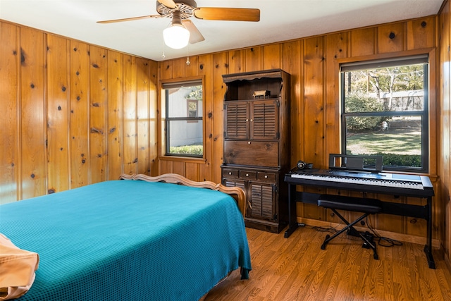 bedroom featuring multiple windows, ceiling fan, wood walls, and hardwood / wood-style flooring