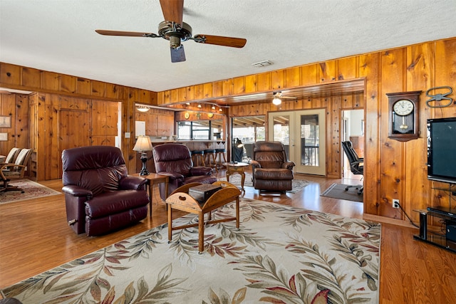 living room featuring hardwood / wood-style flooring, ceiling fan, wood walls, and french doors