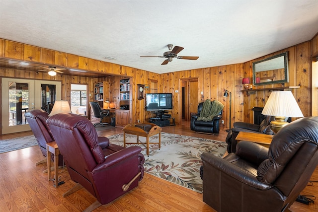 living room with wooden walls, hardwood / wood-style floors, ceiling fan, and french doors