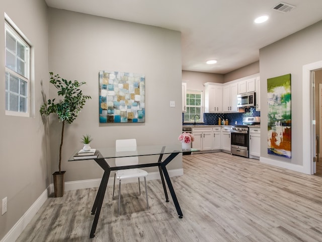 kitchen with appliances with stainless steel finishes, tasteful backsplash, sink, light hardwood / wood-style flooring, and white cabinetry