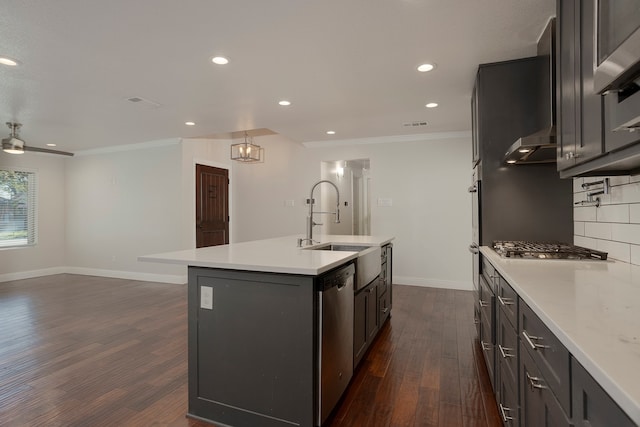 kitchen with wall chimney range hood, dark hardwood / wood-style flooring, crown molding, an island with sink, and appliances with stainless steel finishes