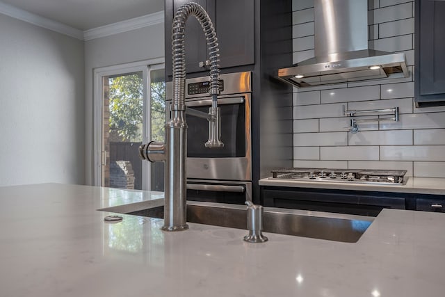 kitchen with light stone countertops, tasteful backsplash, ornamental molding, wall chimney exhaust hood, and stainless steel gas cooktop