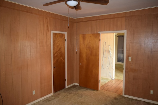 unfurnished bedroom with wooden walls, carpet flooring, ceiling fan, ornamental molding, and a closet