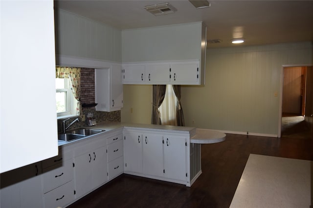 kitchen with kitchen peninsula, backsplash, sink, white cabinets, and dark hardwood / wood-style floors