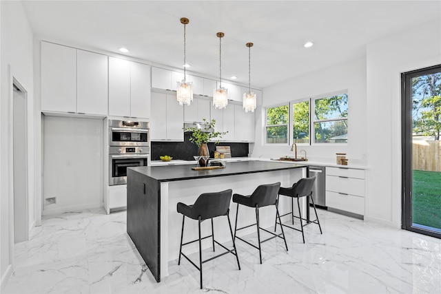 kitchen featuring pendant lighting, appliances with stainless steel finishes, white cabinetry, a kitchen island, and decorative backsplash