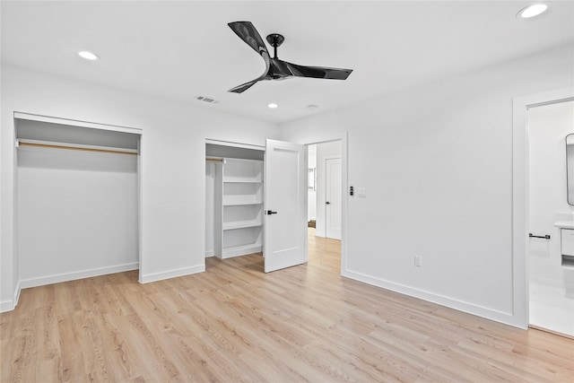 unfurnished bedroom featuring multiple closets, ensuite bath, ceiling fan, and light wood-type flooring