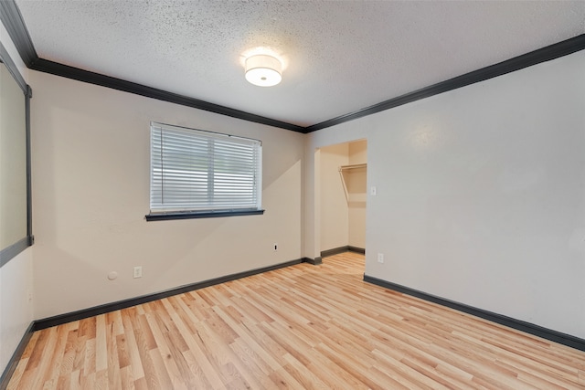 empty room with light wood-type flooring, a textured ceiling, and ornamental molding