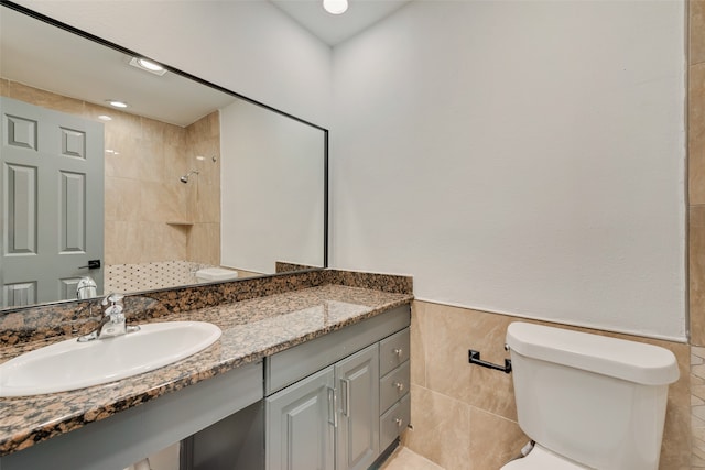 bathroom featuring vanity, toilet, a tile shower, and tile walls