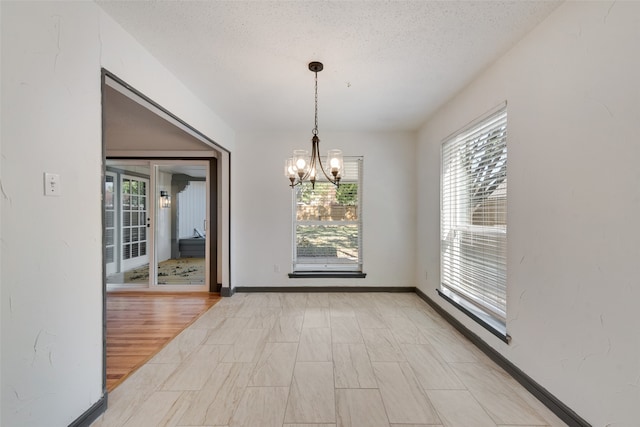 unfurnished dining area featuring a textured ceiling, plenty of natural light, a notable chandelier, and light hardwood / wood-style flooring