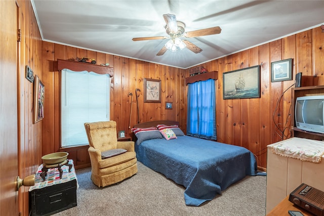 carpeted bedroom with ceiling fan, wood walls, and ornamental molding