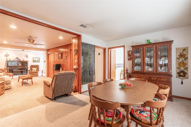 carpeted dining space featuring ceiling fan and wooden walls